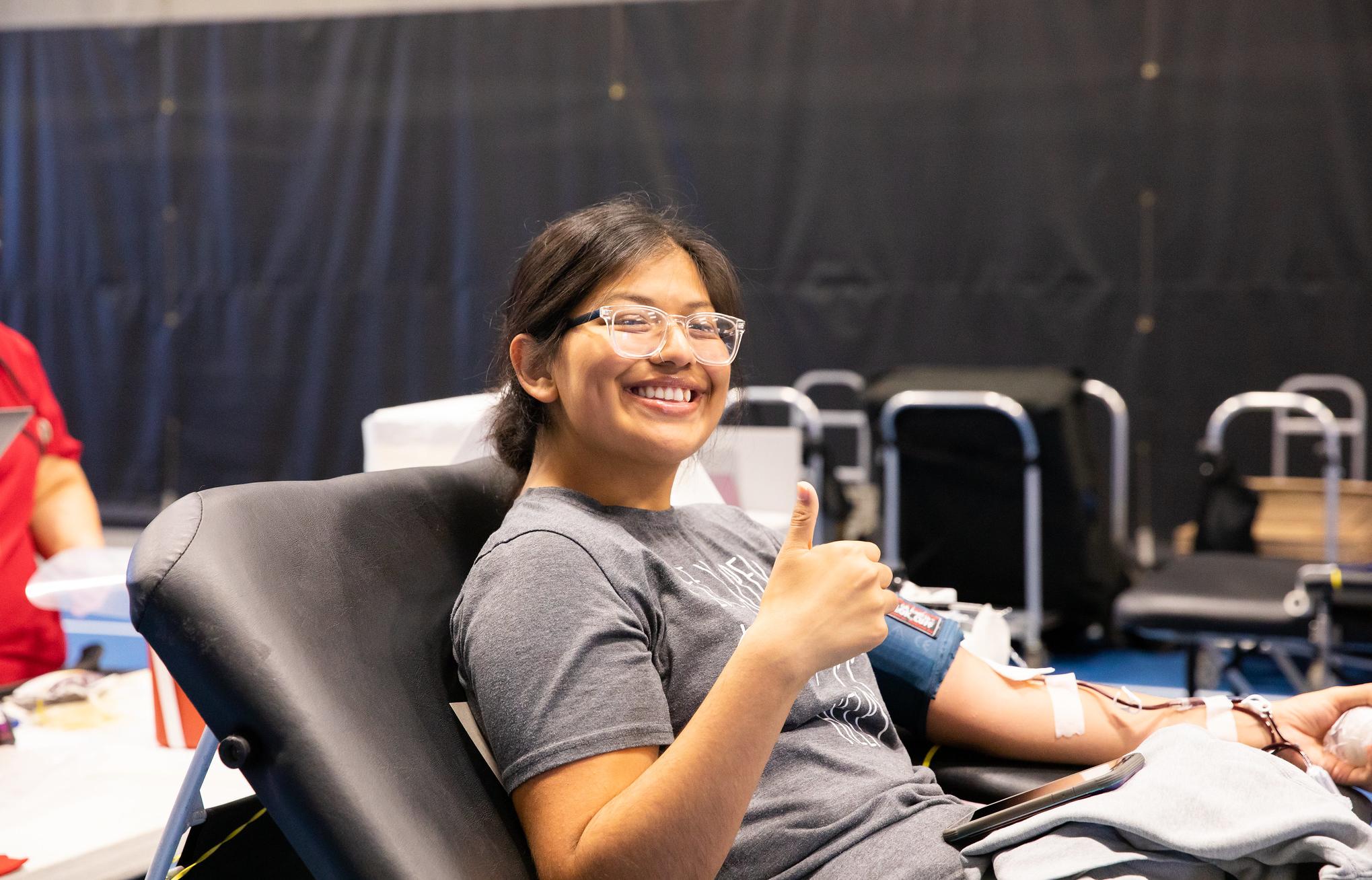a student gives a thumbs up while donating blood