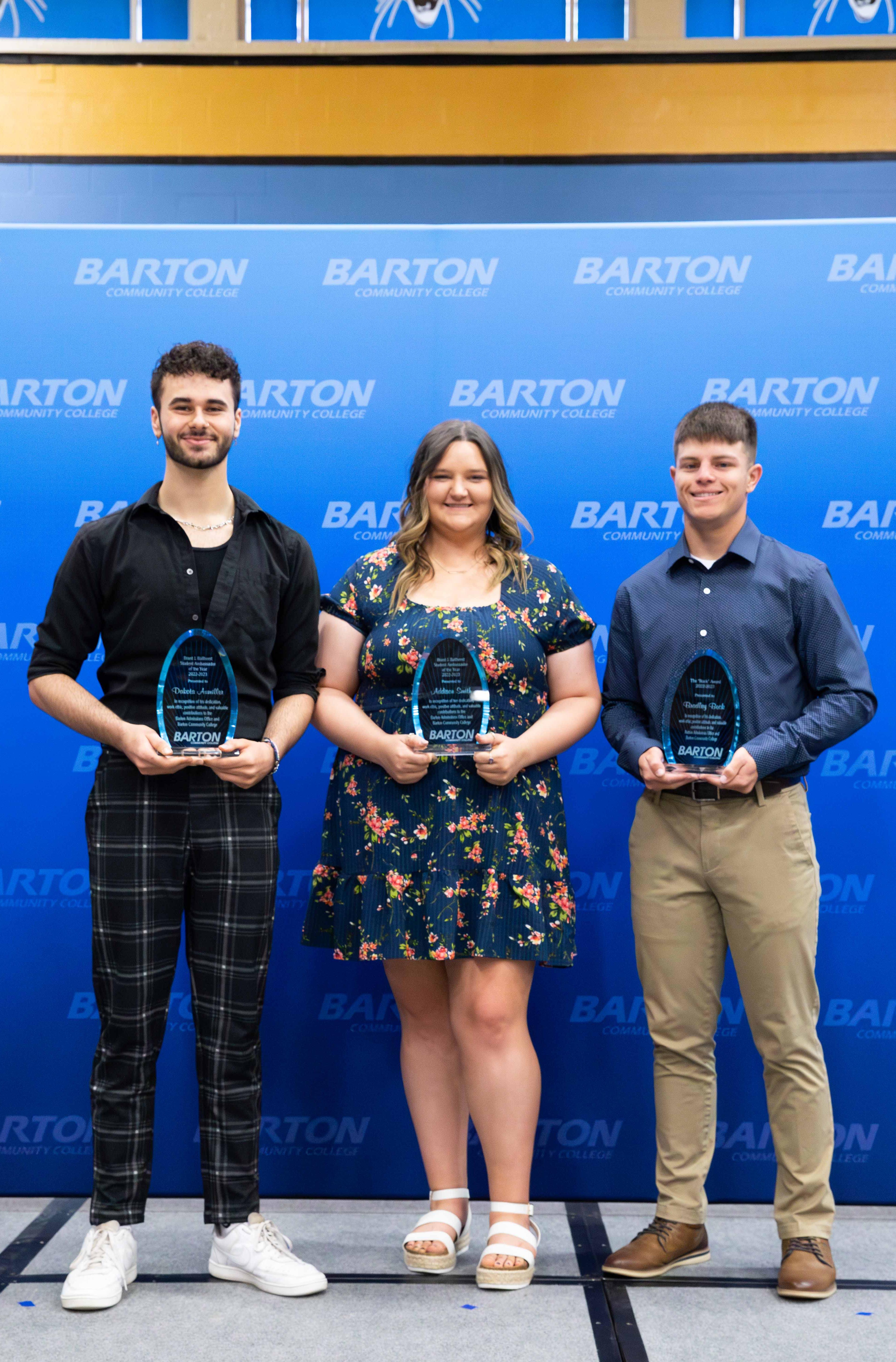 3 people holding awards in front of a blue backdrop